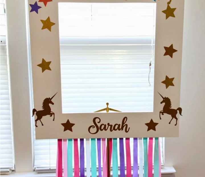 DIY Unicorn Photo Booth Frame with gold unicorn cutouts, colorful stars, and pastel ribbon streamers for a magical birthday party