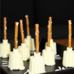 Witch’s broomstick cheese snacks made from mozzarella cheese and pretzel sticks, arranged on a black tray for a Halloween party