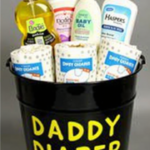 A black bucket labeled 'Daddy Diaper Duty' in bold yellow letters, filled with baby essentials such as diapers, baby oil, lotion, soap, and wipes. A humorous and practical Father's Day gift basket for new dads